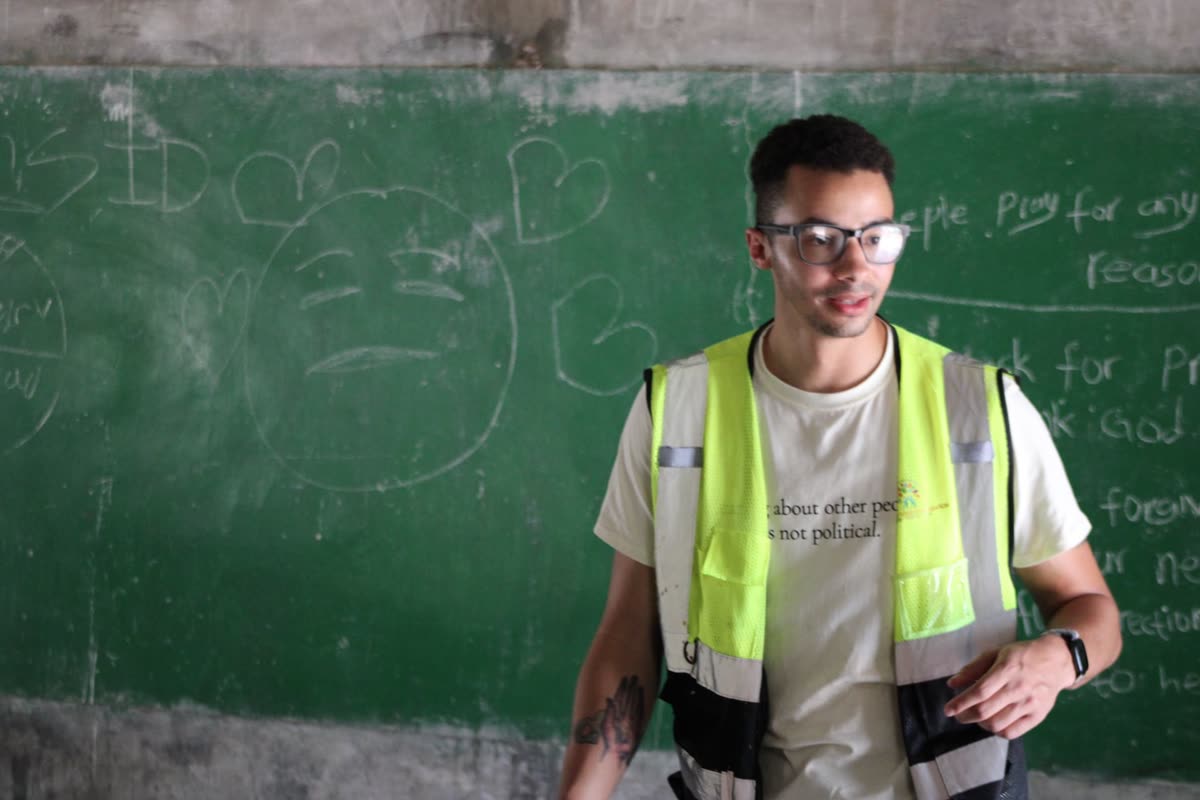 A Dreamers Wish volunteer in a safety vest leads a class in front of a chalkboard